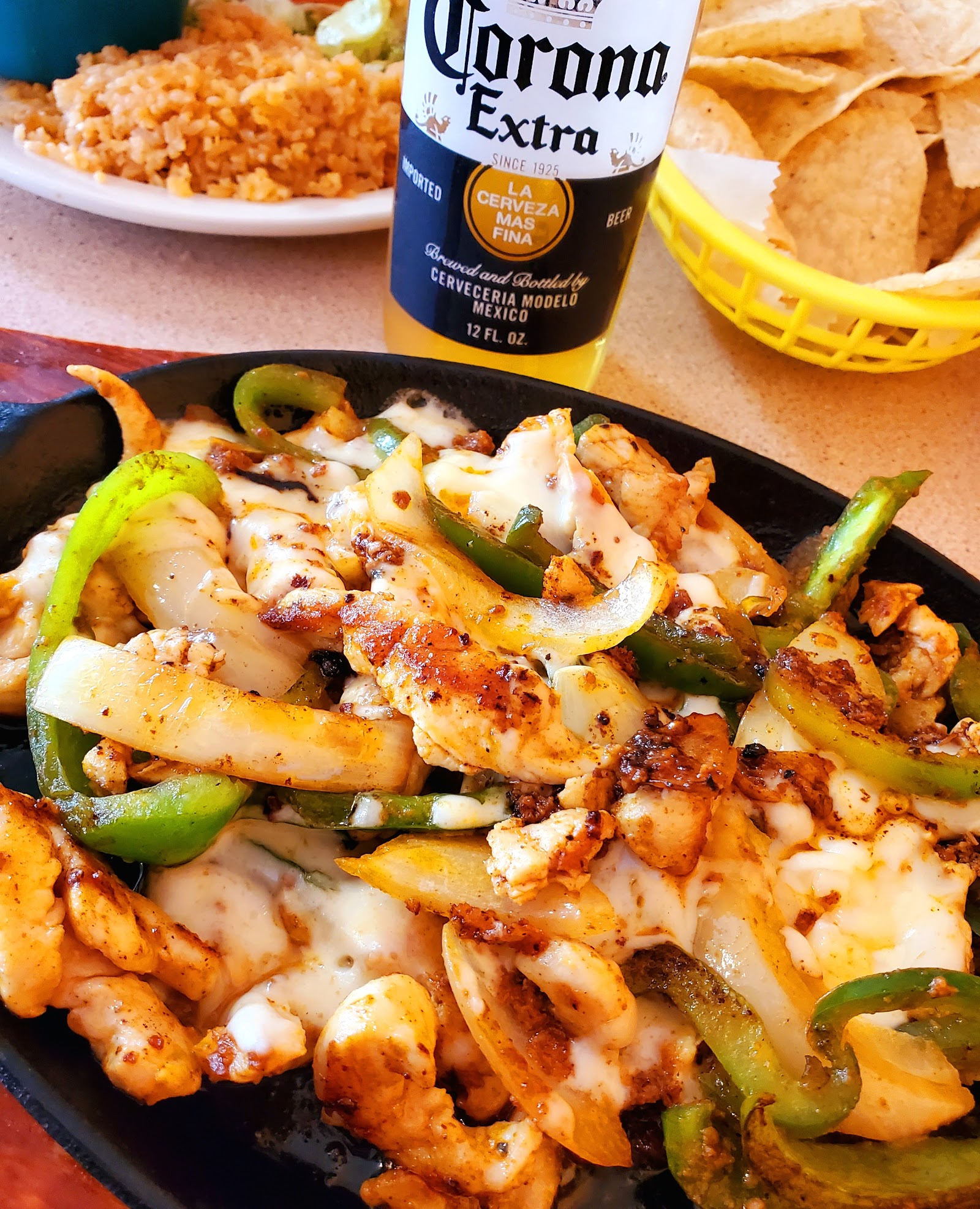 Sizzling skillet fajitas with melted cheese and a Corona Extra